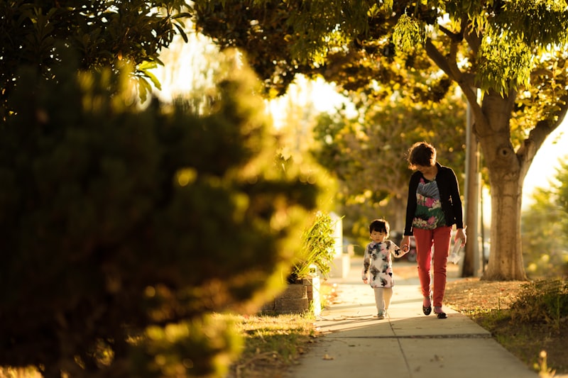 אמא מחזיקה יד של ילדה בשביל מואר באור שמש, הגנה וחום